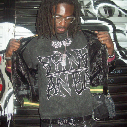 Person wearing a graphic t-shirt with text and design, standing against a graffiti-covered wall.