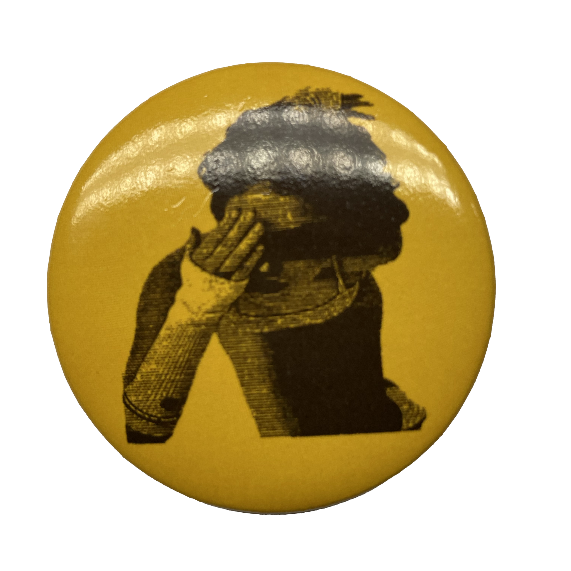 A round brooch pin with a yellow background and a black and white image of a person's profile wearing a hat.