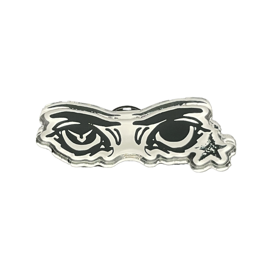A silver-colored acrylic pin with a soft PVC clutch, featuring a stylized eye design behind a mask-like border.